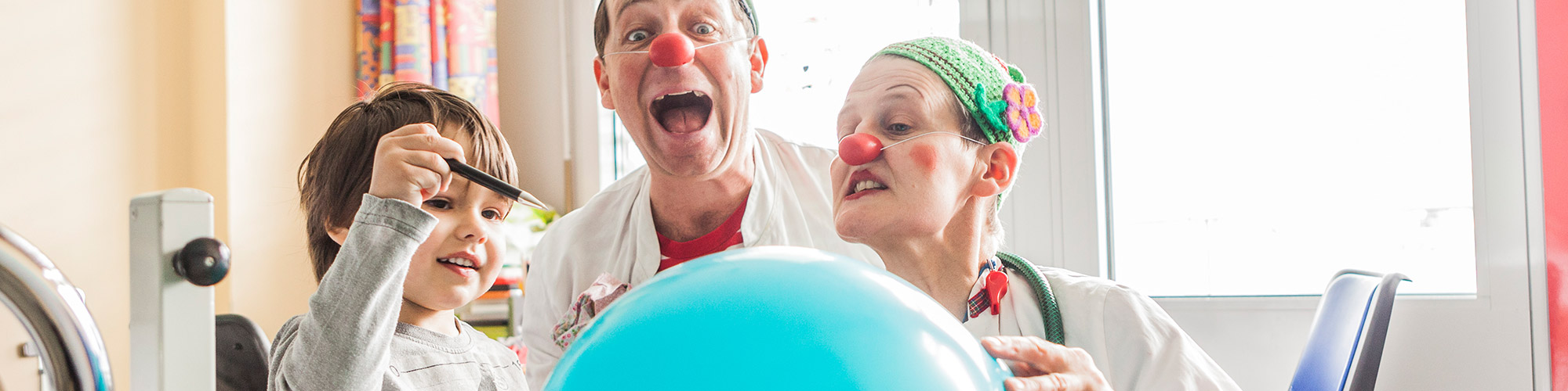 KlinikClowns mit Kleinkind und Luftballon