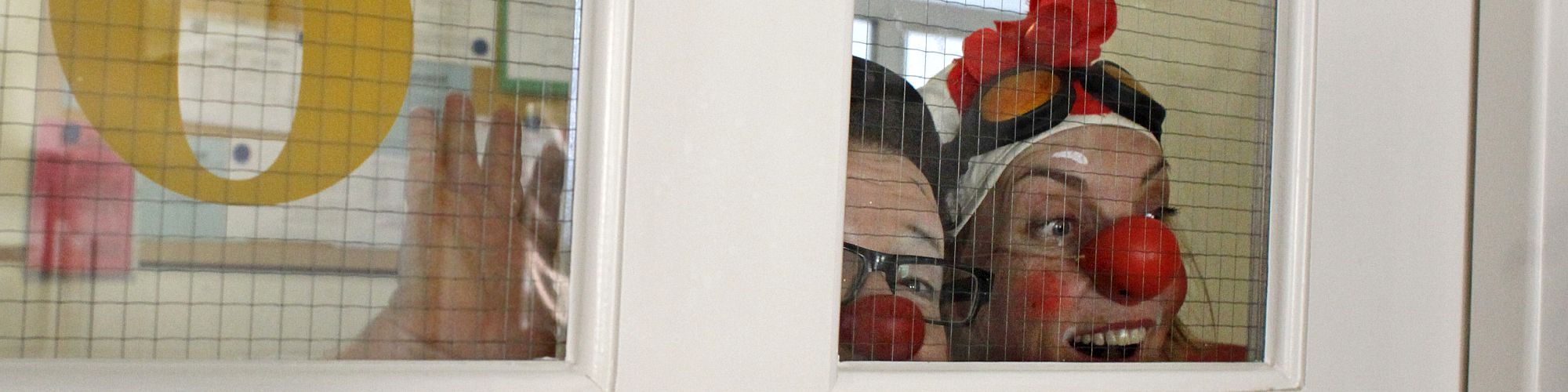 KlinikClowns schauen durch Krankenhausfenster